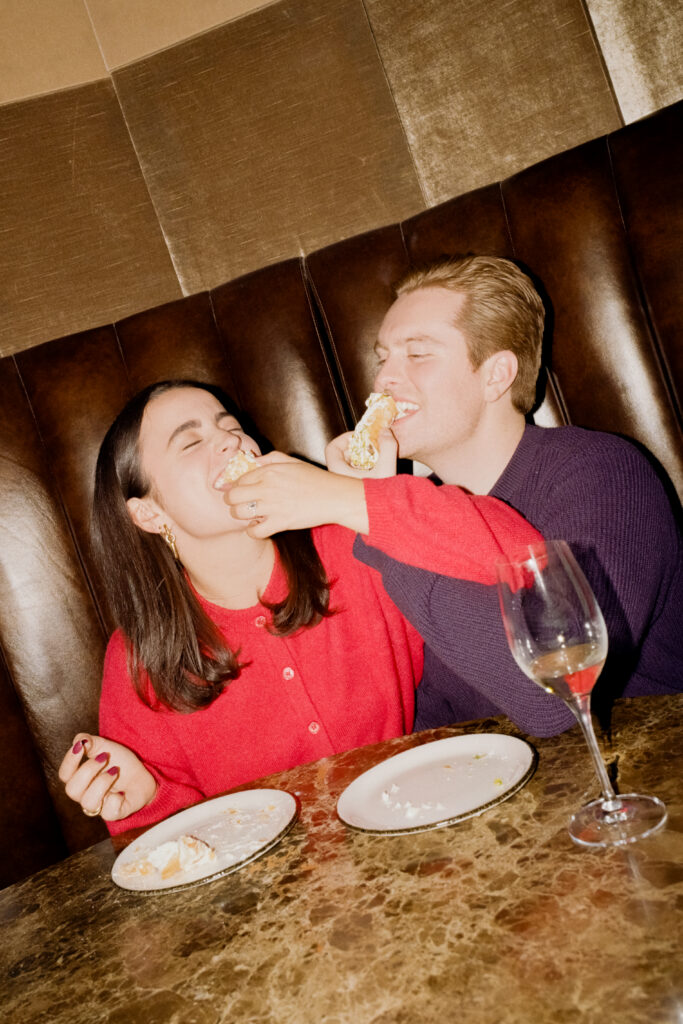 couple eating cake with wine and taking a bite with arms crossed 