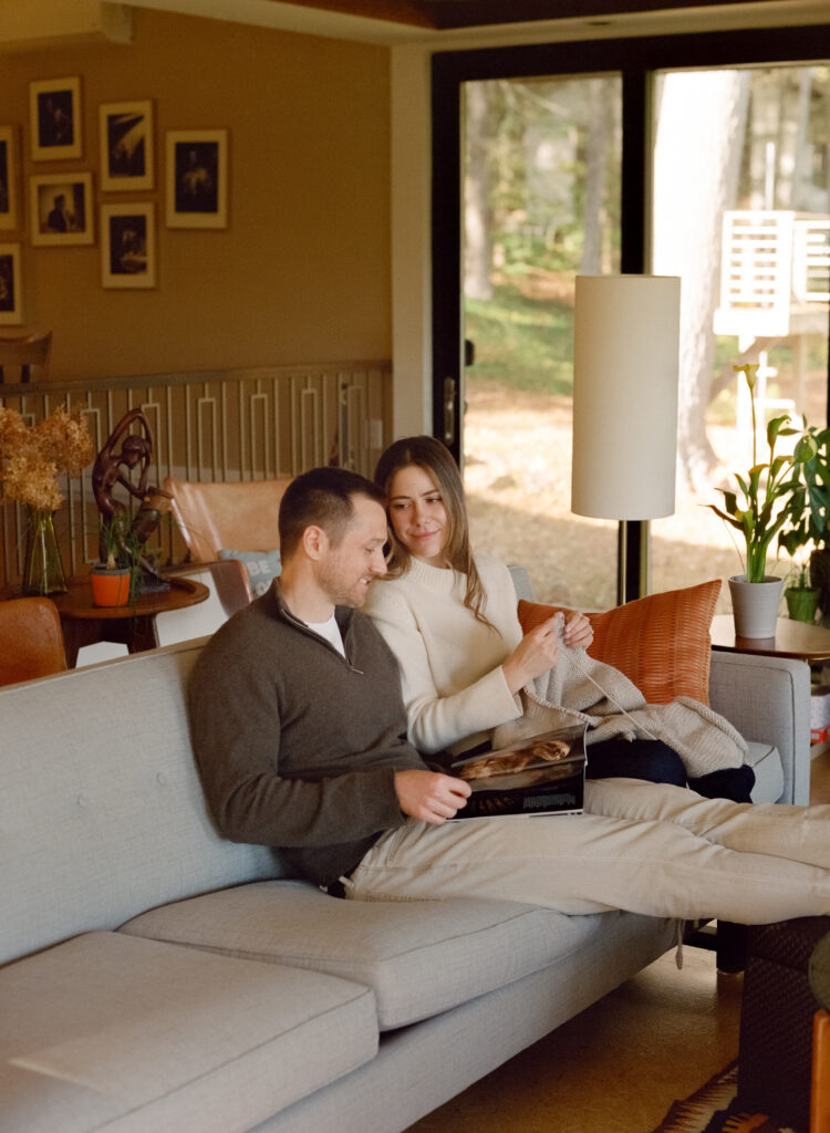 man sitting on the couch reading a magazine next to a women knitting a sweater 