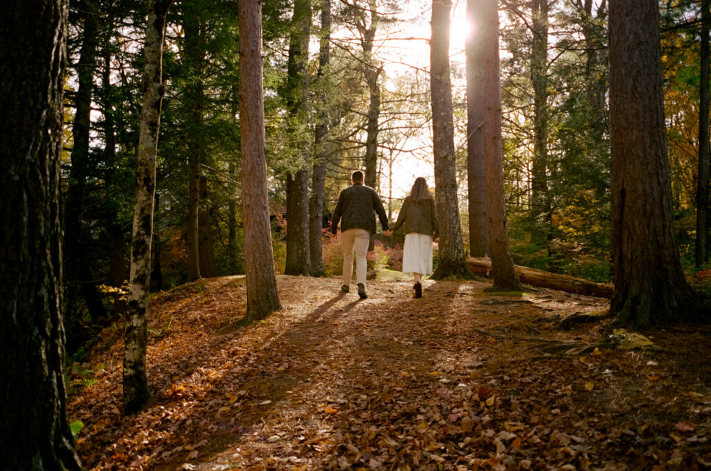 couple walking through woods holding hands with sun shining down
