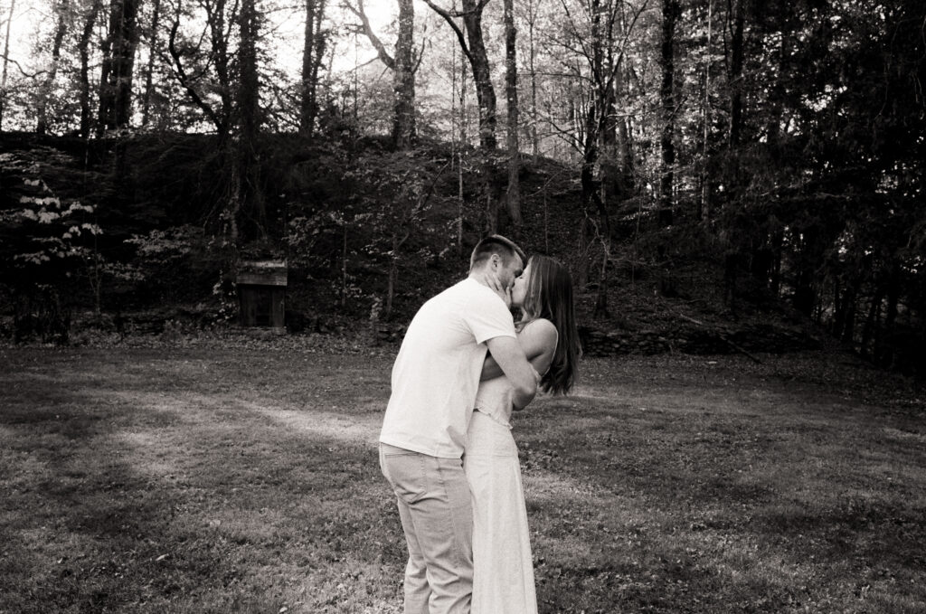 couple hugging and kissing in the woods in black and white photo