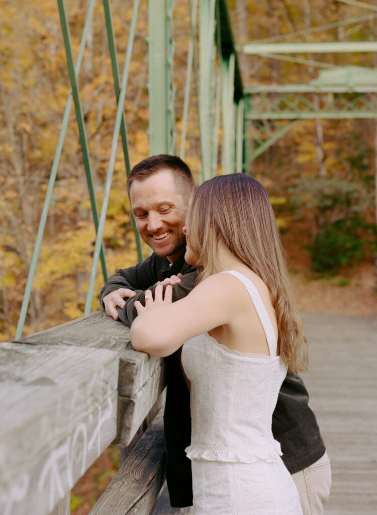 couple smiling lovingly at each other on bridge during fall