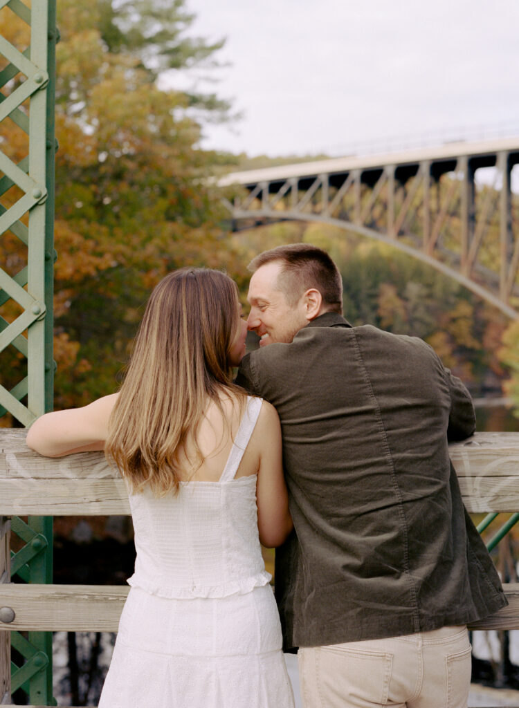 couple smiling lovingly at each other on bridge during fall