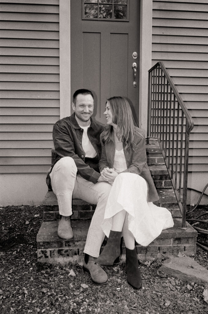 couple laughing and smiling on front porch during film engagement photos 