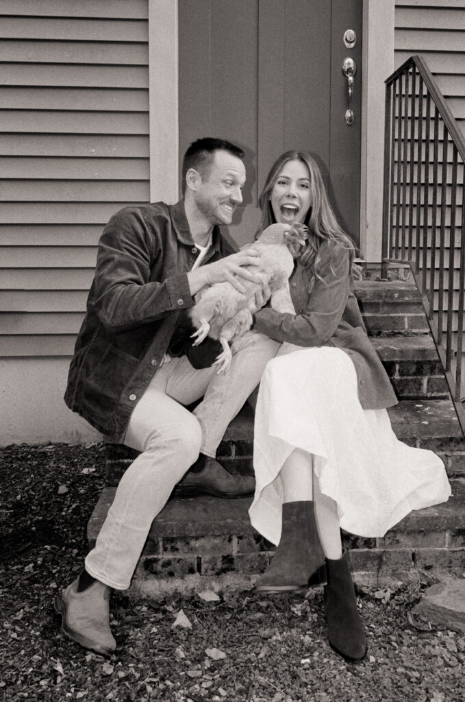 couple holding a chicken laughing on a porch 