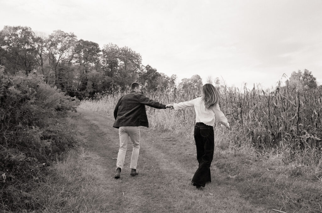 couple running in field holding hands  in film engagement photos 