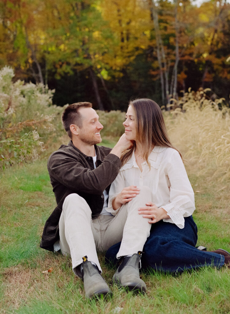 couple snuggling in a field during personalized film engagement photos 