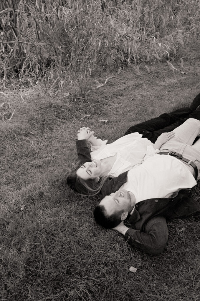 couple laying down smiling and cuddling in a field 