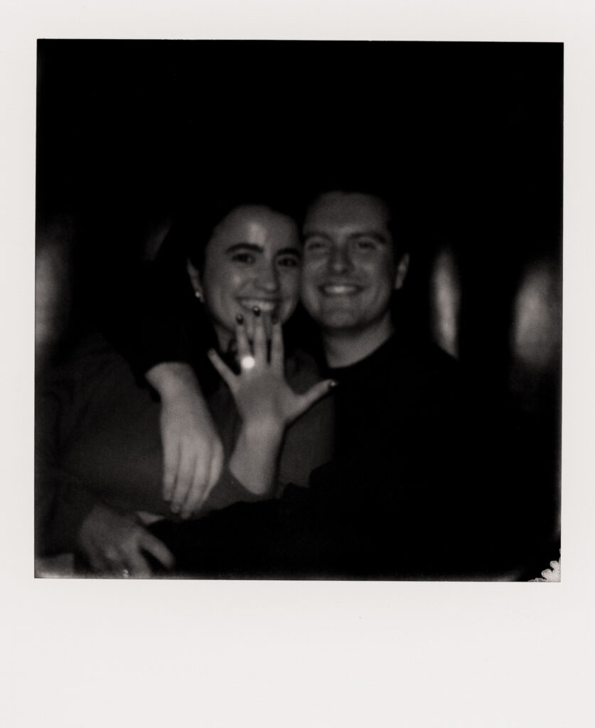 polaroid photo of couple smiling showing off engagement ring 