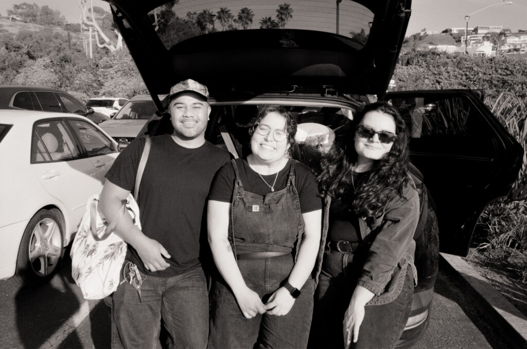 three people smiling behind a car with the trunk open