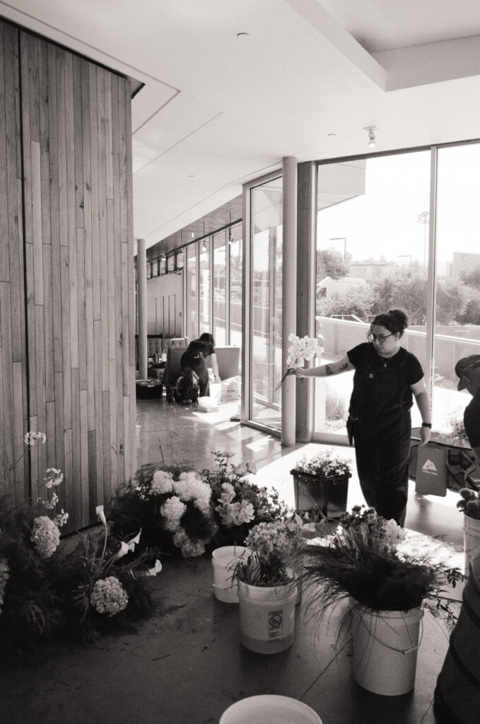 a woman holding flowers in a room full of flowers in buckets for a Scripps Seaside Forum wedding 