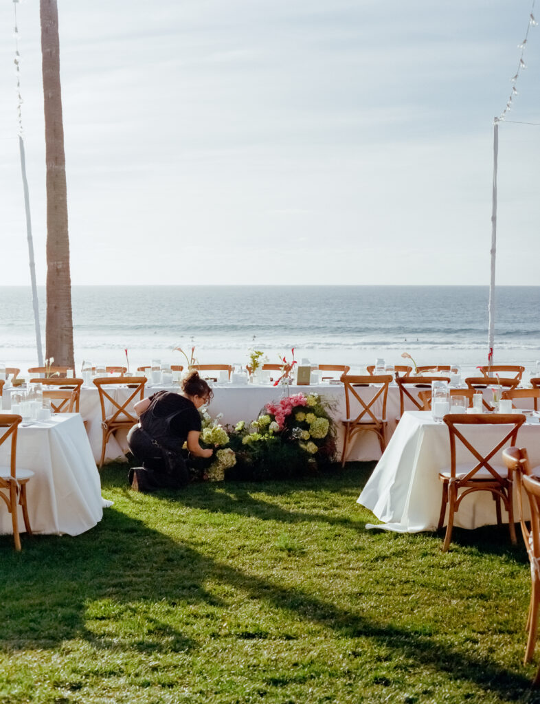 woman working with flowers at the beach with wedding tables 