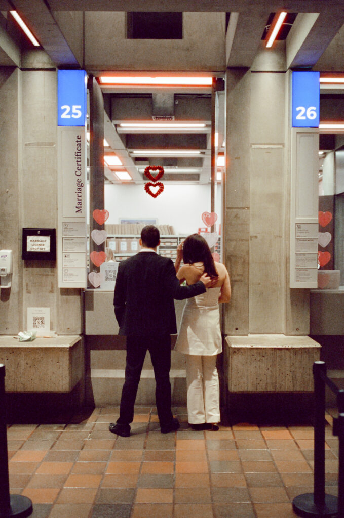 a man has a hand on a woman's back in front of the marriage certificate desk at the Boston City Hall
