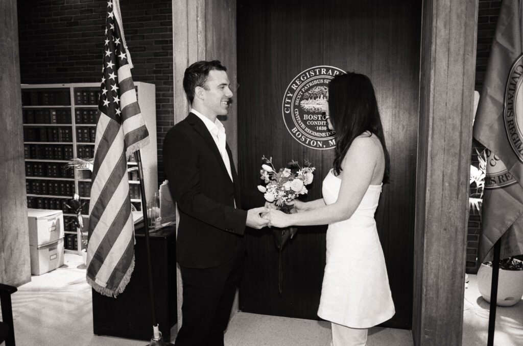 Man and woman standing in the Boston City Hall holding hands while saying their vows