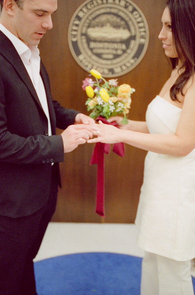 woman staring lovingly at her soon to be husband and he places a wedding ring on her finger during a Boston City Hall elopement 