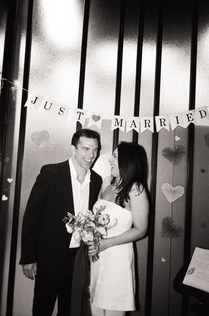 Man and woman holding a bouquet standing in front of a just married sign during their Boston City Hall elopement 
