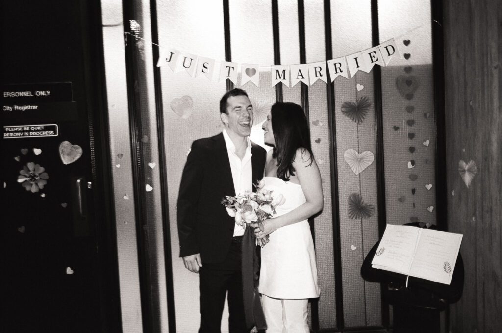 Man and woman holding a bouquet standing in front of a just married sign during their Boston City Hall elopement 