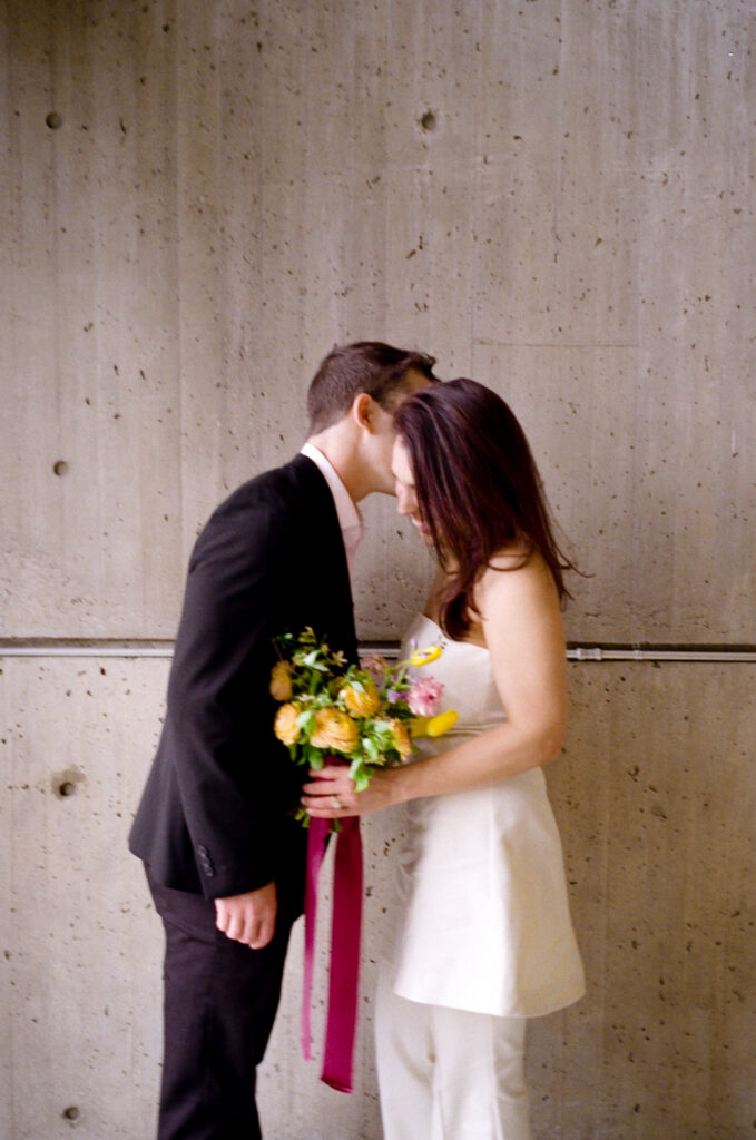 man whispering in woman's ear, making her smile while she holds a wedding bouquet 