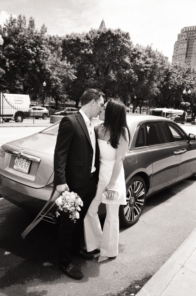 newly married couple kissing in front of luxury car in black and white photos