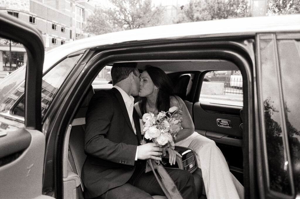 bride and groom kissing at each other in a luxury car leaving the courthouse after their elopement 
