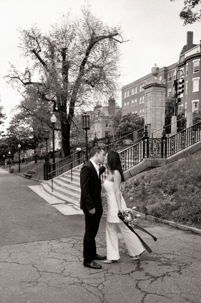 bride and groom leaning in a and kissing while bride holds on to a bridal bouquet in black and white photo 