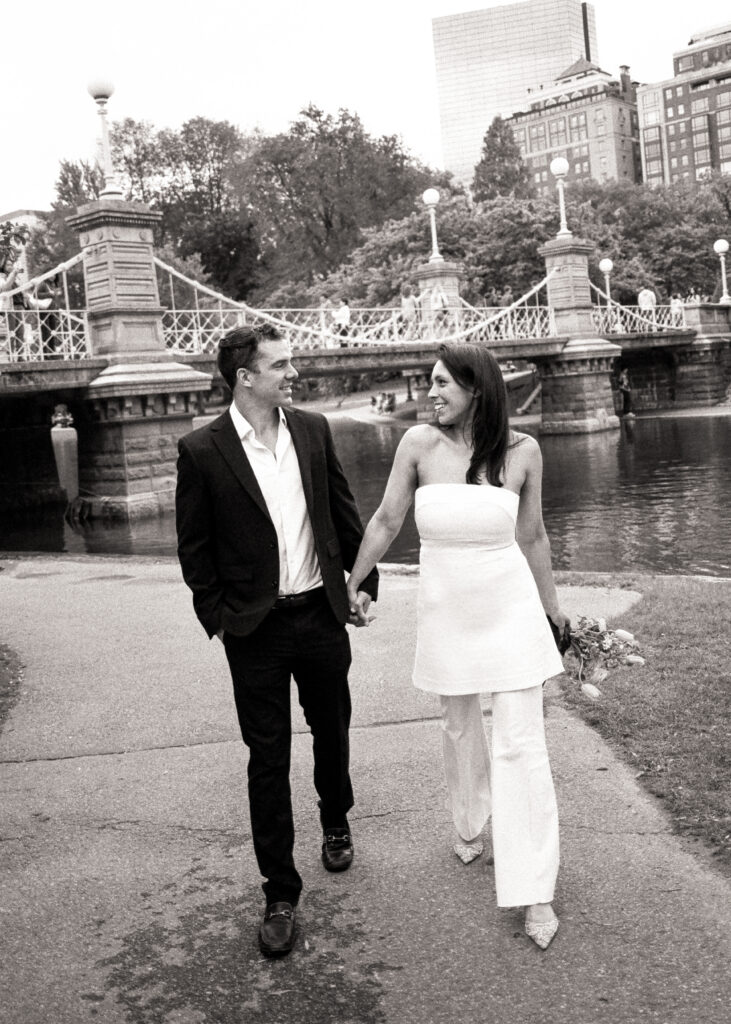 bride and groom walking through park holding hands after their Boston City Hall elopement in black and white photo 