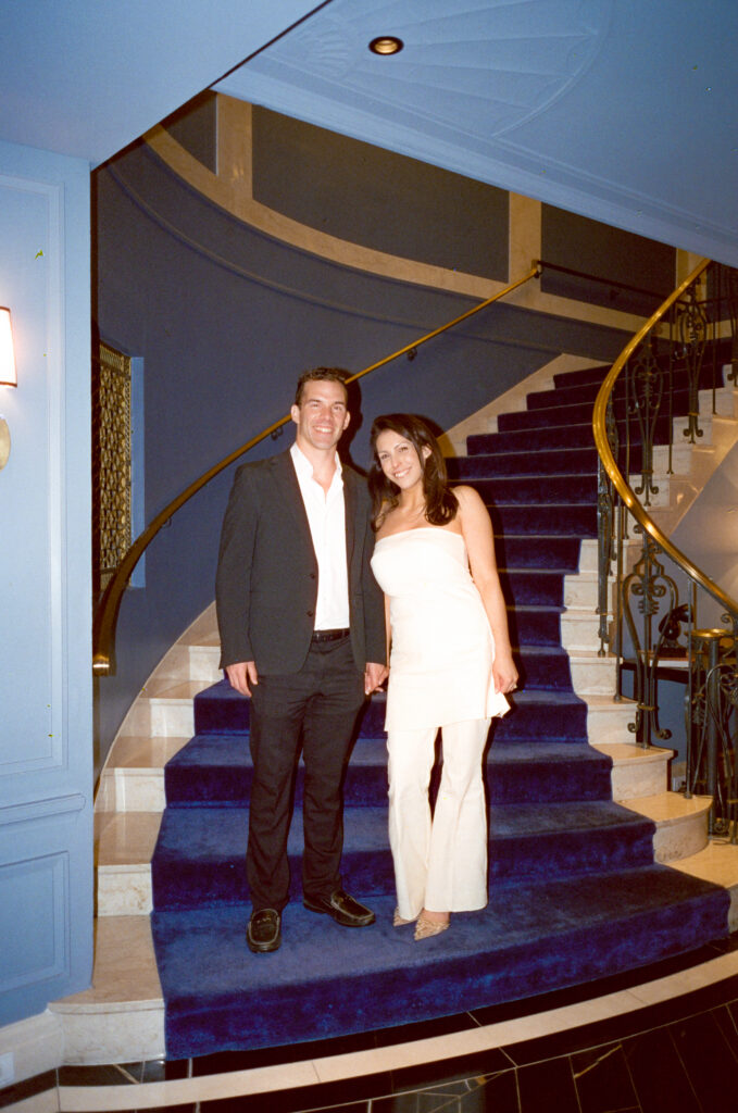 bride and groom standing on velvet blue stairs holding hands and posing for a photo 