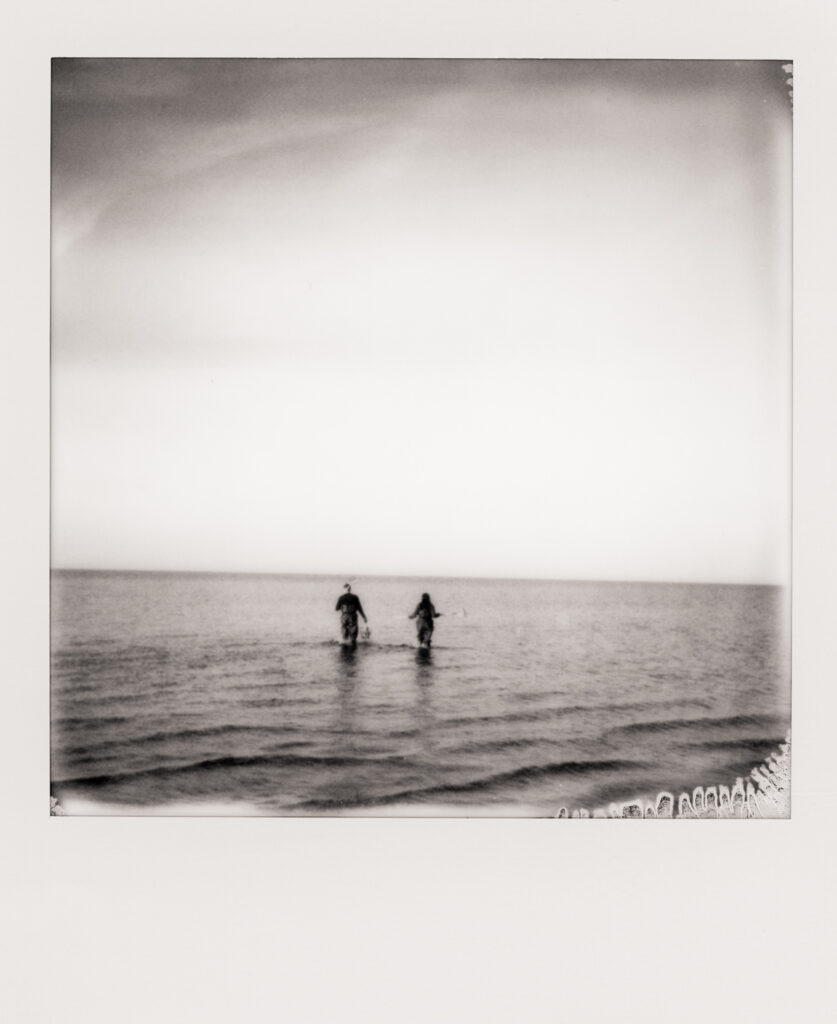 man and women walking out of ocean after clamming during a Cape Cod engagement photos in polaroid photo