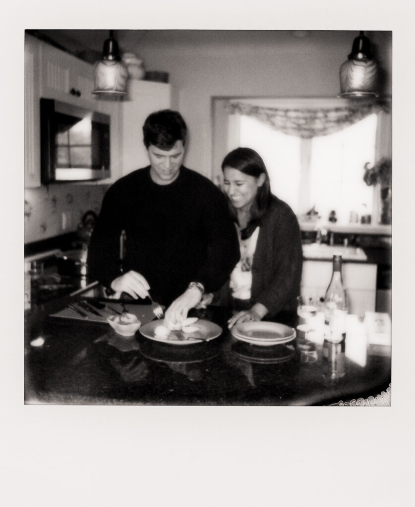 polaroid photo of a couple laughing a cooking clams together in the kitchen