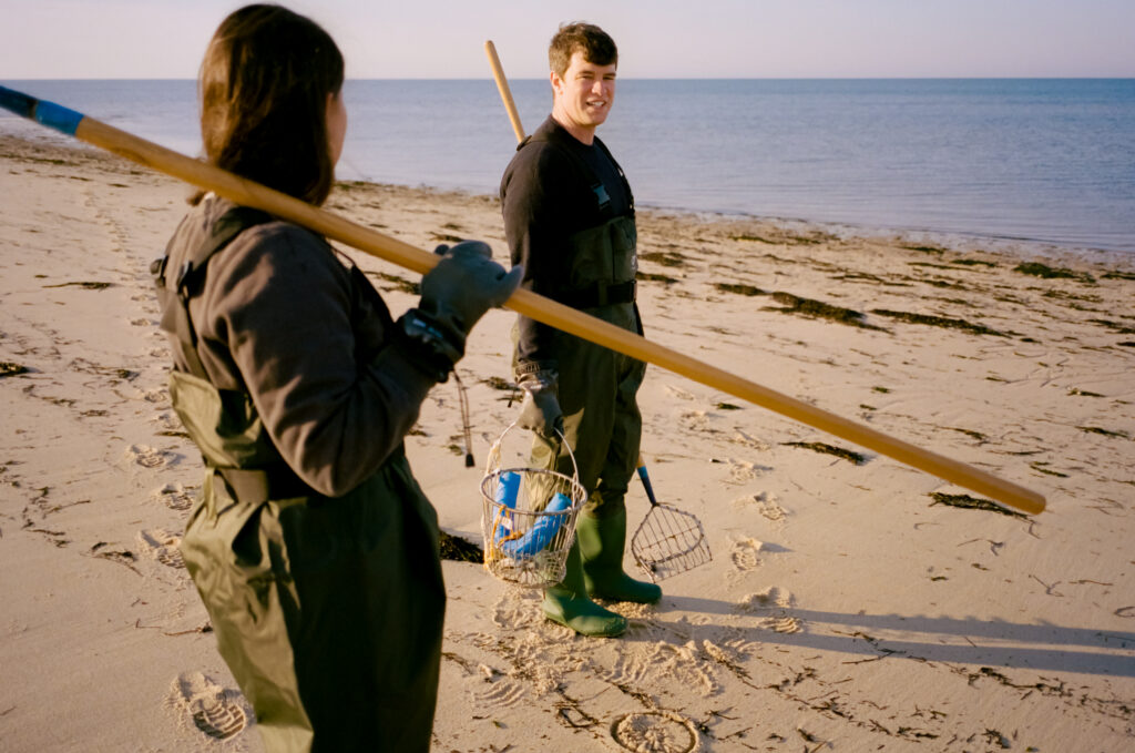 man and women standing on a beach in Cape Cod holding clamming gear during engagement photos