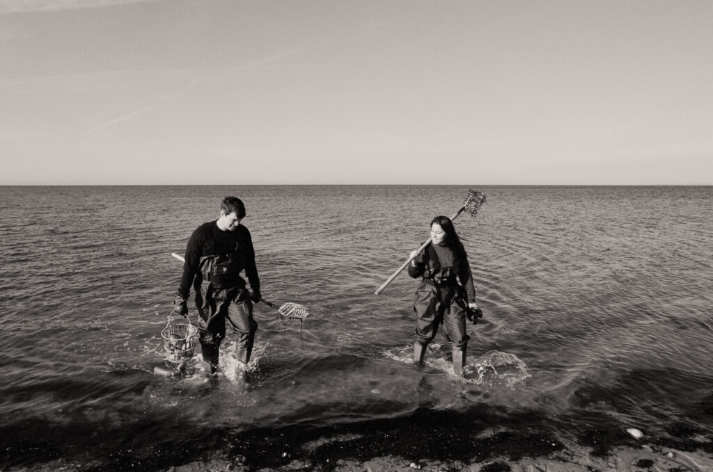 man and women walking out of ocean after clamming during a Cape Cod engagement photos