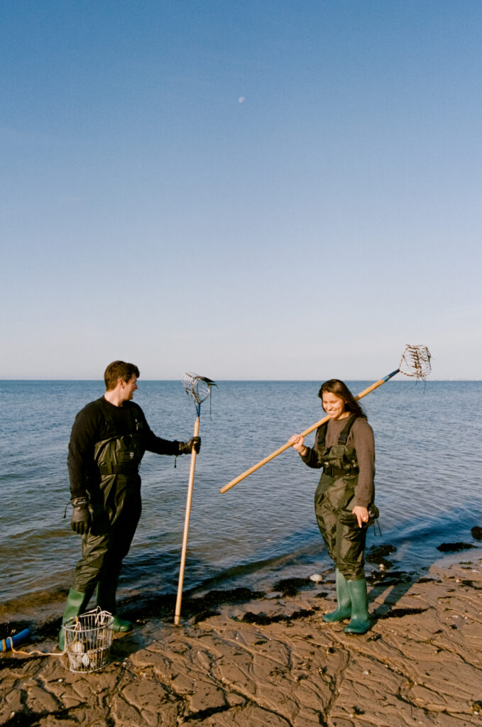 man and women standing on a beach in Cape Cod holding clamming gear during engagement photos
