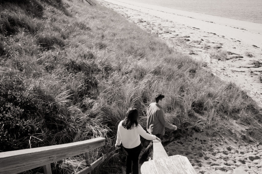 man and women walking down onto the beach in black and white photo during a Cape Cod engagement session