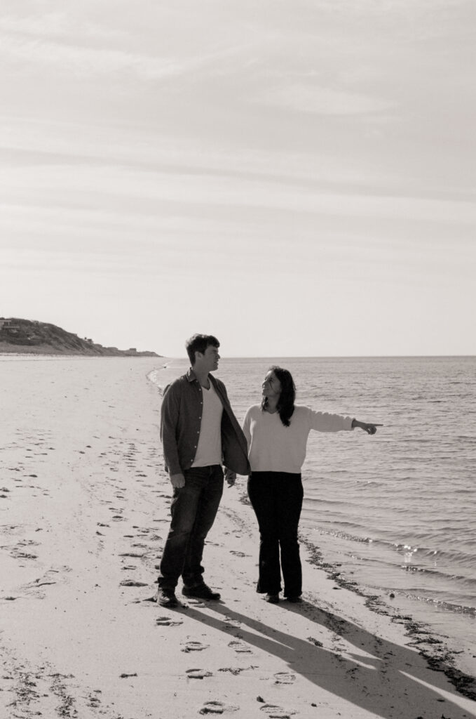 woman holding hands with a man pointing to the ocean on the beach in black and white photo
