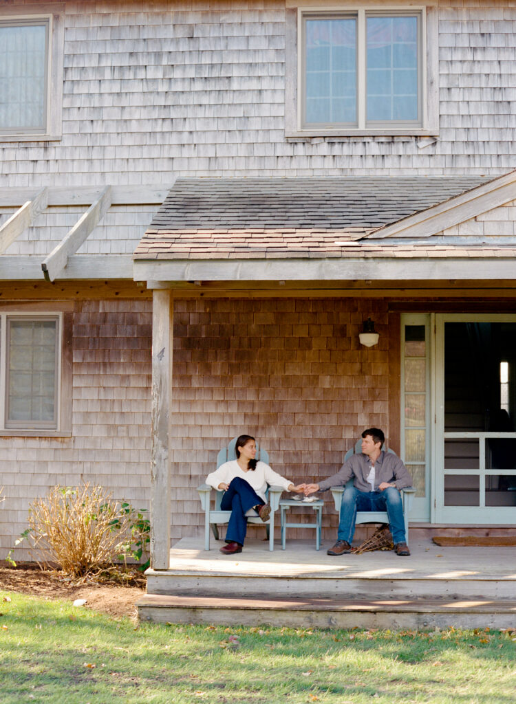 a man and woman holding hands sitting in porch chairs on front porch
