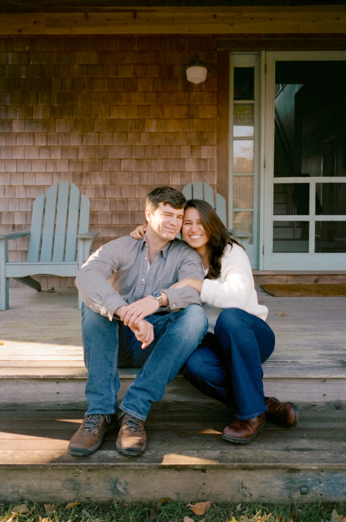 couple hugging on porch in front of house during film engagement photos in Cape Cod