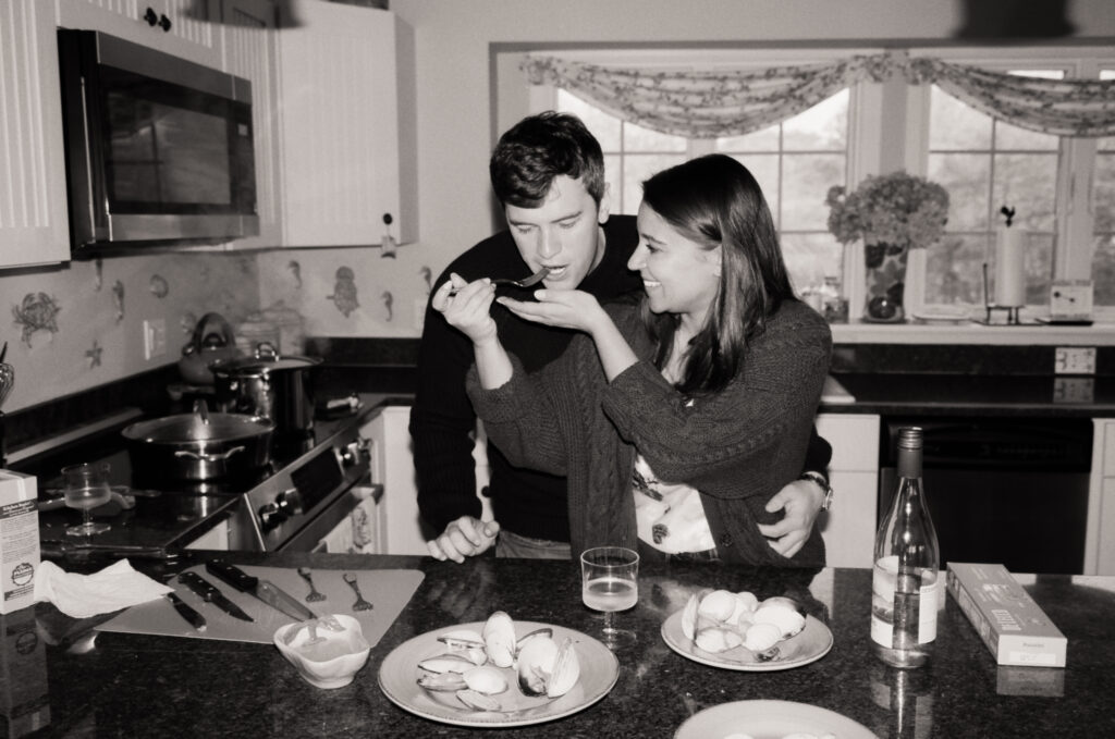 couple laughing a cooking clams together in the kitchen in black and white film photos