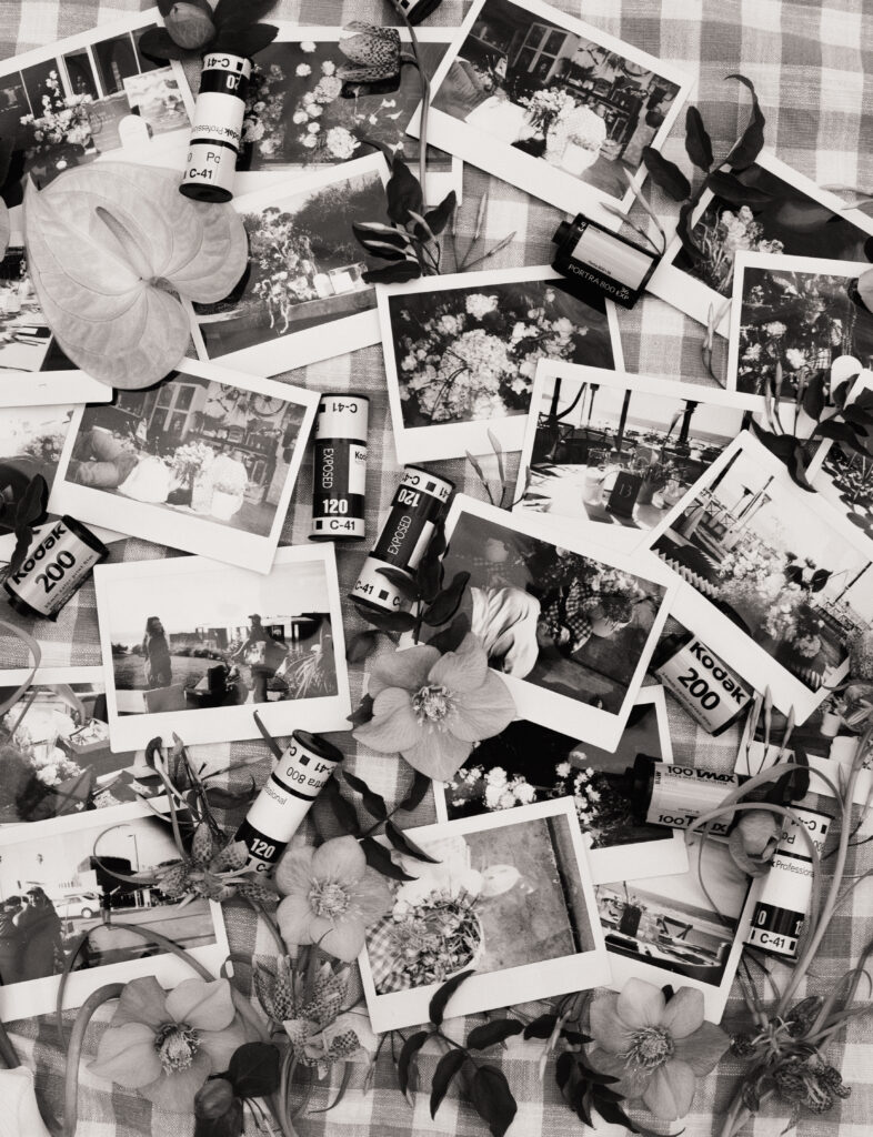 polaroids and film rolls arranged with flowers and greenery in a black and white photo  